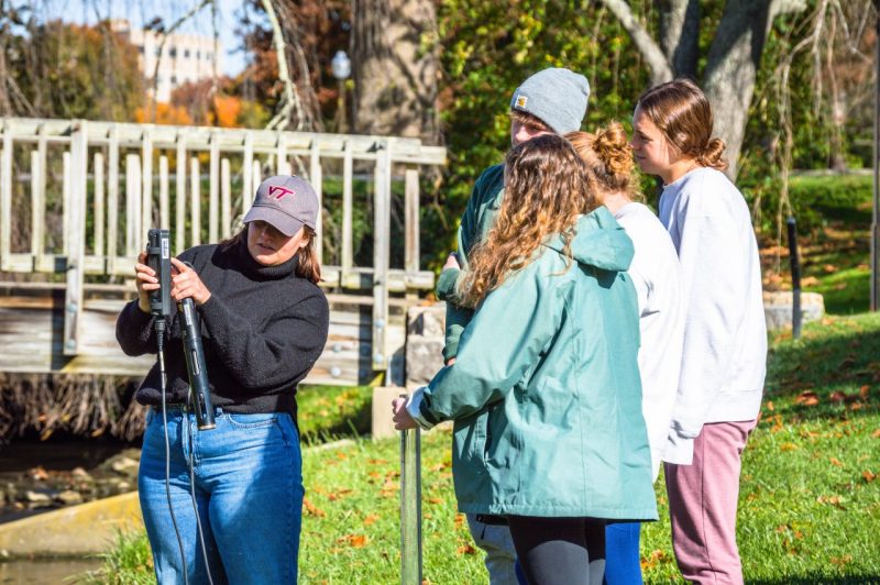 BSE Graduate Student showing group of BSE students how to use a measuring device at Duck Pond on Virginia Tech's campus