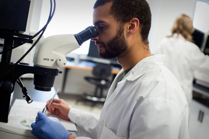 Man in white coat looking into microscope