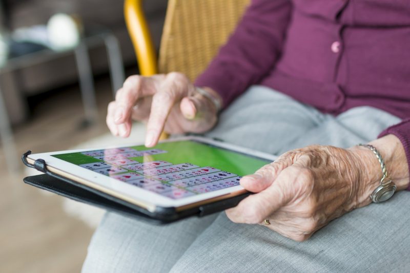 An elderly woman plays solitaire on her tablet.